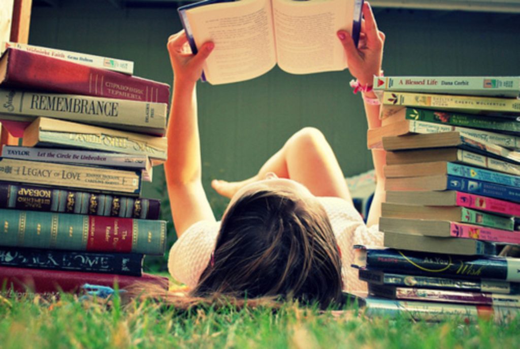 A girl reading a book with a bunch of books beside her. Image Source: Obvious. Bookworms live longer.